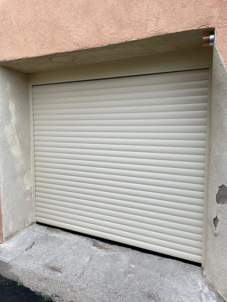 Porte de garage enroulable beige posée dans une ouverture en retrait