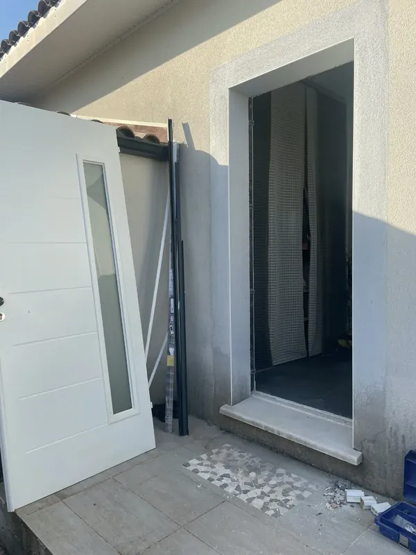 Chantier de pose de porte d'entrée : ouverture dégagée et préparée, nouvelle porte blanche prête à être posée