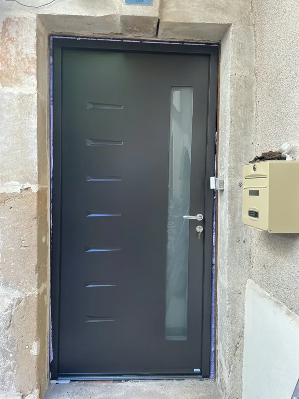 Porte d'entrée contemporaine anthracite posée dans un encadrement en pierre de maison de village, dans l'Hérault