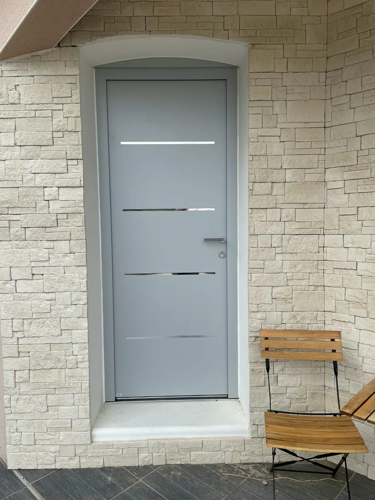 Porte d'entrée grise à inserts inox dans une façade en pierre